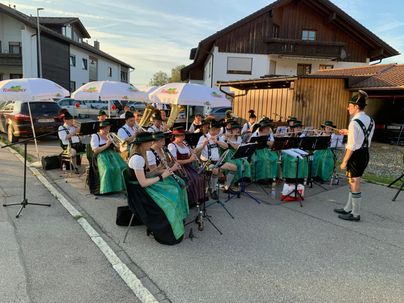 Eine Musikkapelle spielt im Freien, während sie unter Sonnenschirmen steht. Die Musiker tragen traditionelle Kleidung und sind in einer stimmungsvollen Umgebung aufgestellt.
