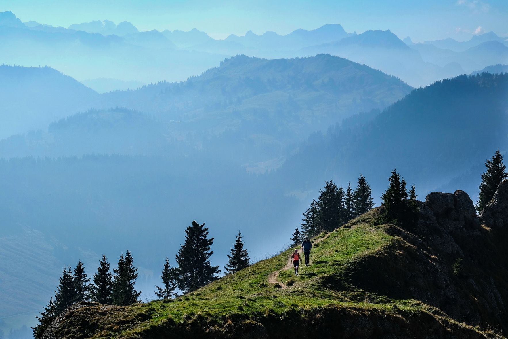 Zwei Bergfreunde wandern entlang eines schmalen Gratwegs entlang der Nagelfluhkette. Im Hintergrund sieht man die Allgäuer Bergwelt. Die Gratwanderung entlang der Nagelfluhkette ist eine beliebte Tour für erfahrene Bergwanderer.