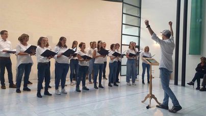 Ein Chor singt in einem modernen Raum. Der Dirigent steht vorne und leitet die Sängerinnen und Sänger.