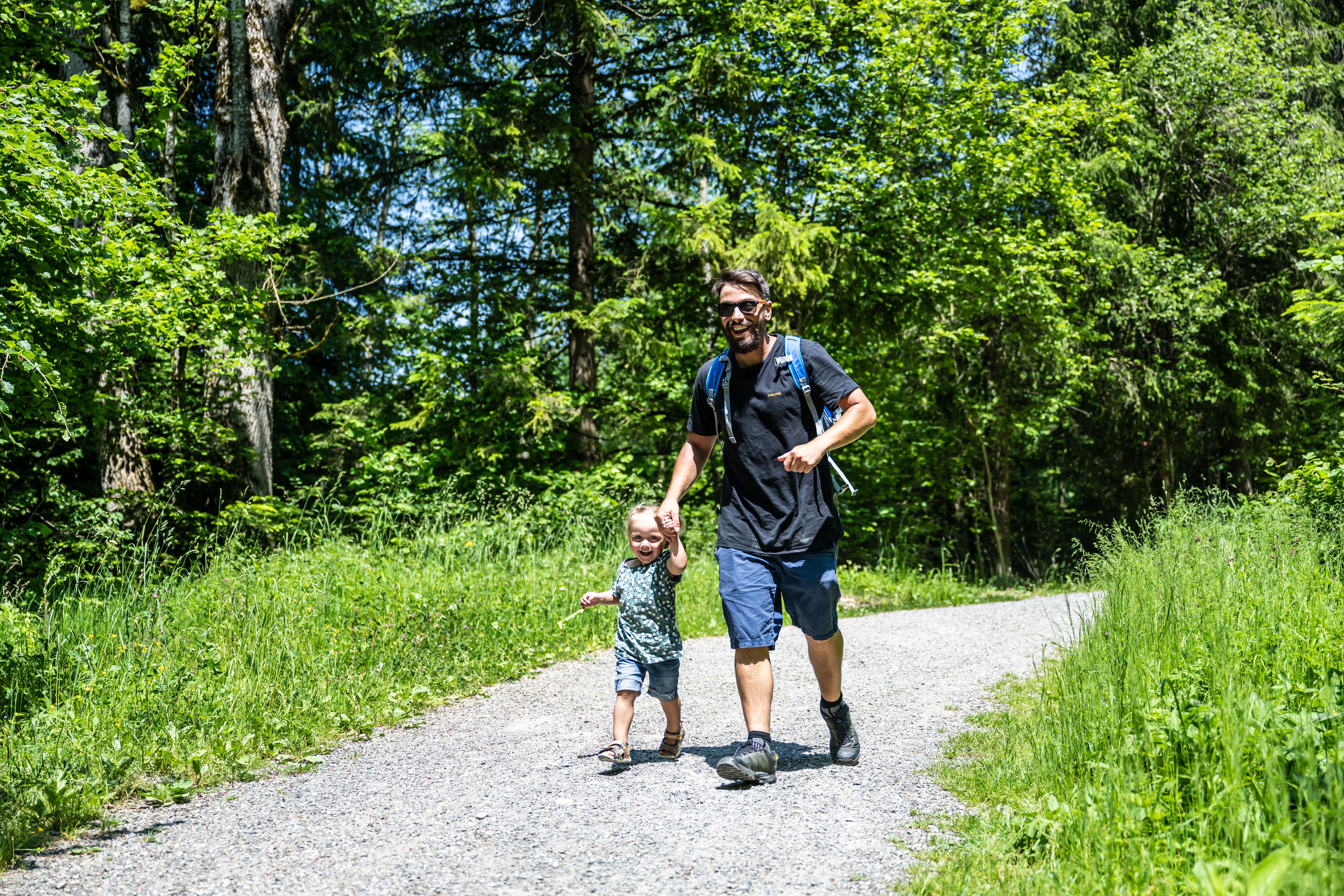 Ein Mann und seine Tochter wandern auf dem 2,6 km langen Rundweg "Erlebnispfad Galetschbach" vorbei an Wiesen und Bäume.