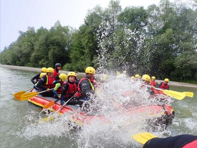 Eine Gruppe von Rafting-Abenteurern in einem Boot auf einem Fluss. Wassertropfen spritzen hoch, während sie durch die Strömung paddeln.