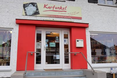Ein Geschäftseingang mit rotem Rahmen und weißen Wänden. Über der Tür hängt ein Schild mit der Aufschrift „Karfunkel“.