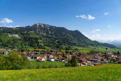 Winter Ortsansicht von der Gemeinde Rettenberg mit dem Grünten und den Allgäuer Hochalpen im Hintergrund.