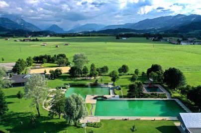 Luftaufnahme auf das Naturbad Familien-Vitalpark in Burgberg. Bei einem Naturbad handelt es sich um ein künstlich an­ge­legtes, naturnahes Freibad. Das Wasser hier in Burgberg wird durch biologisch-mechanische Prozesse ohne Einsatz von Chlor oder Ähnlichem aufbereitet. Der Familien-Vital-Park Blaichach-Burgberg bietet für Gäste jeden Alters Spaß und Erholung.