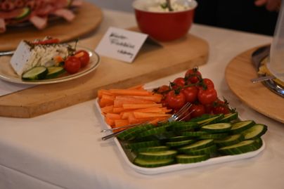 Ein platter mit frischem Gemüse, einschließlich Karotten, Kirschtomaten und Gurken. Im Hintergrund sind weitere Gerichte und eine Schale sichtbar.