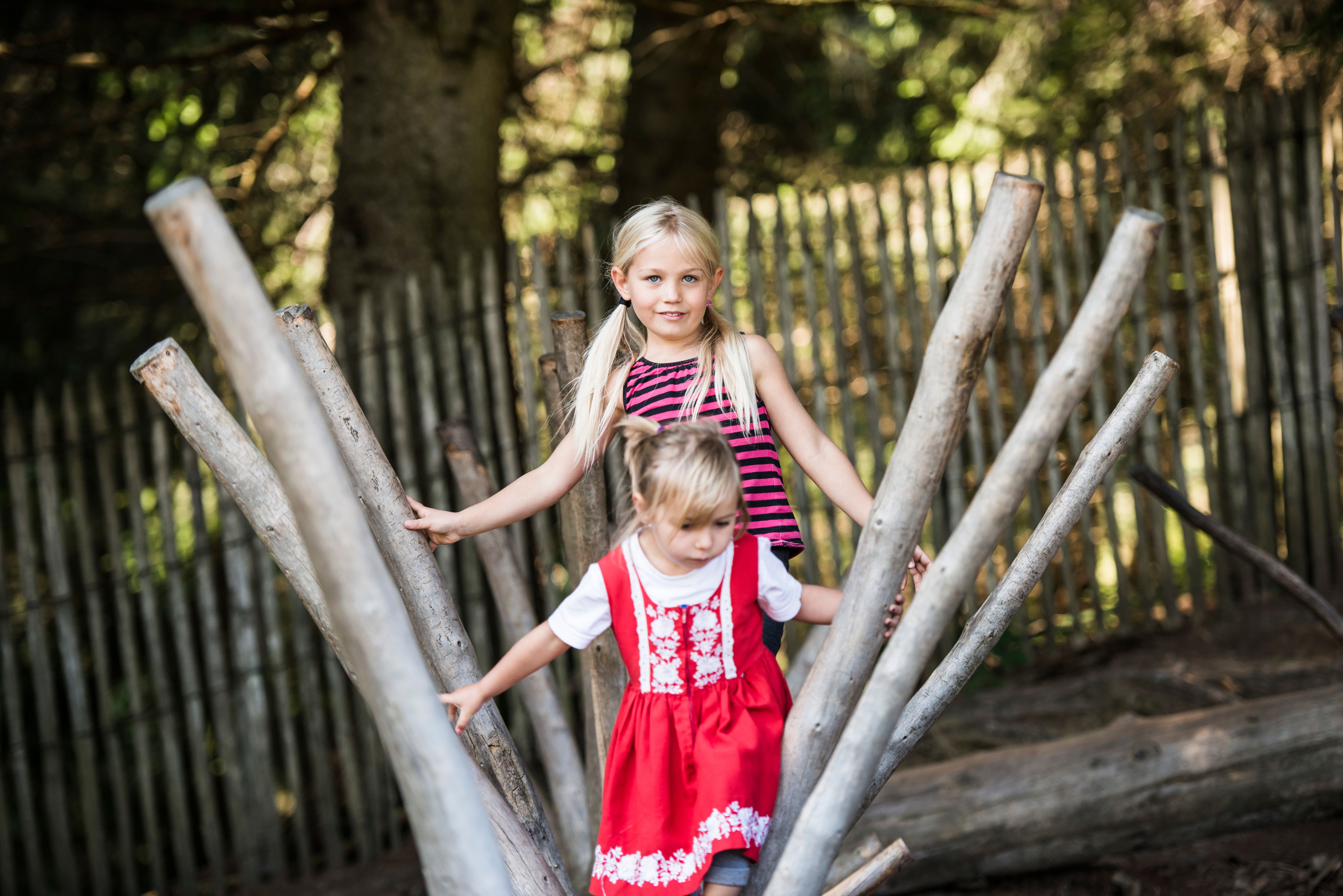 Zwei Mädchen klettern auf einem Holzgerüst. Der Spielplatz liegt im Wald.