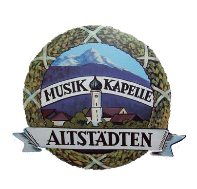 Ein dekoratives Schild mit dem Text "Musik Kapelle Altstädten". Im Hintergrund sind Berge und ein Kirchturm zu sehen.