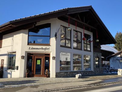 Ein charmantes Gebäude mit traditioneller Architektur und dekorierten Fenstern. Die Straße vor dem Haus ist schneebedeckt und die Umgebung wirkt ruhig und einladend.
