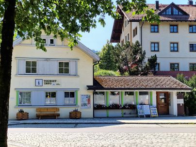Ein hübsches Tourismusinformationsgebäude mit einer einladenden Vorderseite. Im Hintergrund sind weitere Gebäude und Bäume zu sehen.