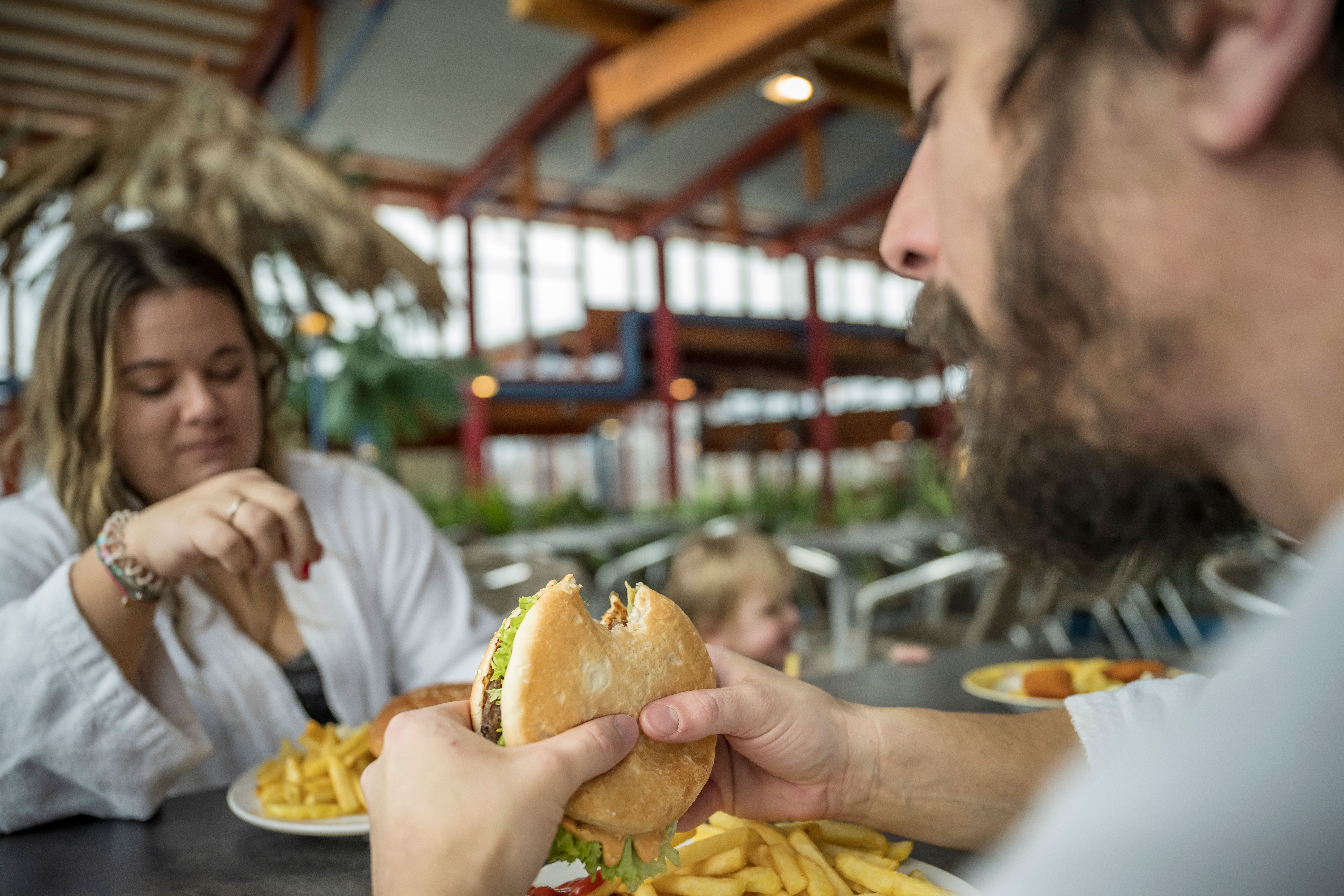 Ein Paar genießt gemeinsam im Palmengarten des Wonnemar Sonthofen einen Burger mit Pommes.