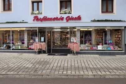 Ein Geschäft für Parfums mit einer einladenden Fensterfront. Draußen stehen Tische mit bunten Blumen und Dekorationen.