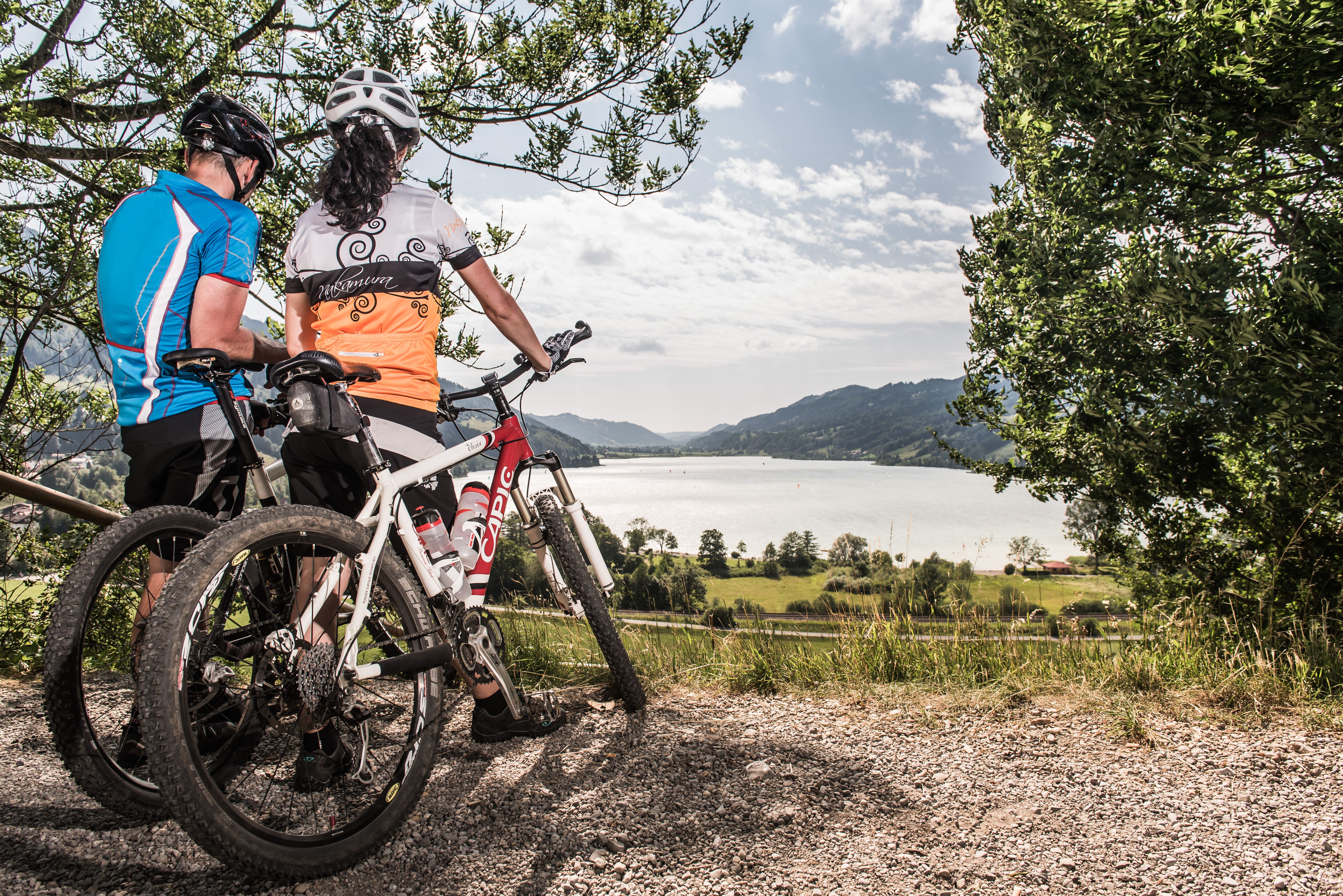 Ein Paar steht mit seinen Fahrrädern im Sommer in Immenstadt mit Blick direkt über dem Alpsee.