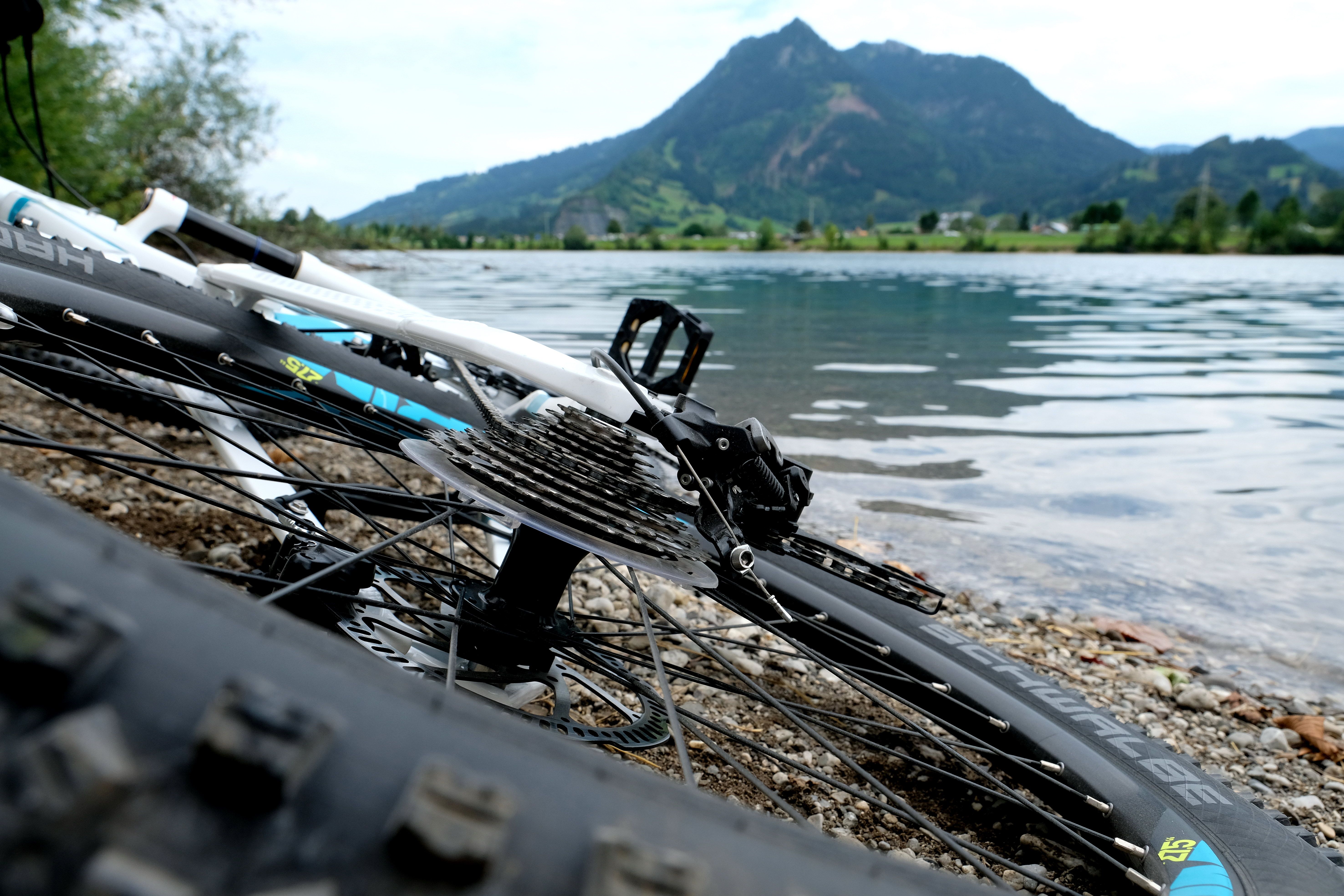 Ein weißes Fahrrad liegt am Ufer eines Sees. Im Hintergrund liegt der Grünten.