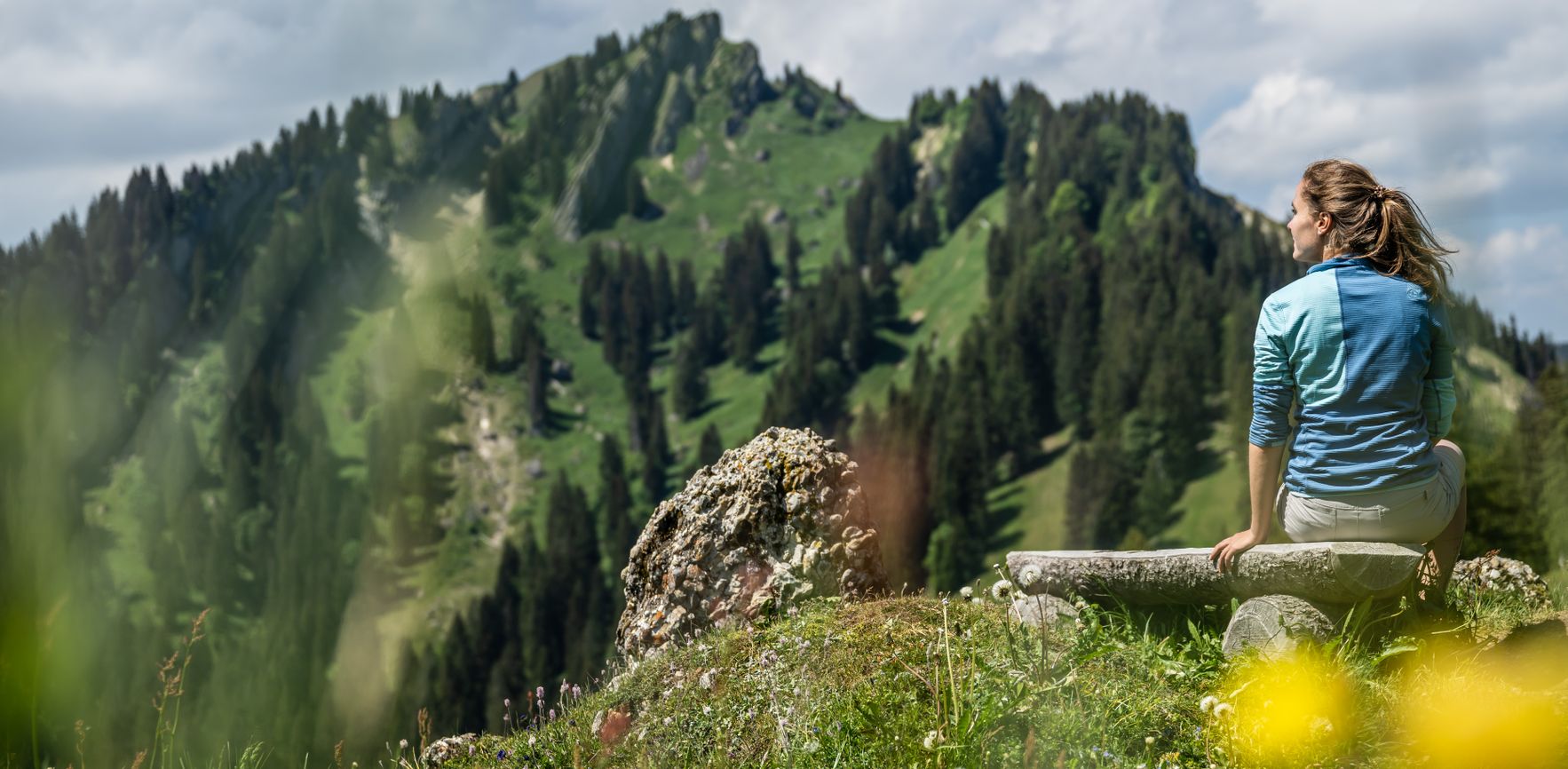 Eine Frau macht während einer Wanderung auf einer Bank mit Blick auf den Steineberg Rast.