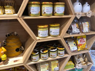 Ein Regal mit verschiedenen Honiggläsern und Bienenprodukten. Die Gläser sind in einem bienenwabenförmigen Holzregal angeordnet.