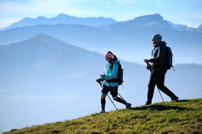 Zwei Wanderer wandern mit ihren Stöcken über die Nagelfluhkette. In der Ferne erstrecken sich die Allgäuer Alpen. Die reizvolle und sehr anspruchsvolle Gratwanderung über die Nagelfluhkette ist die Königsdisziplin in der Alpsee-Grünten Region.