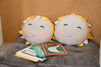 Zwei fröhliche Kissen in Sonnenform auf einer weichen Unterlage. Neben ihnen liegen mehrere kinderfreundliche Bücher.