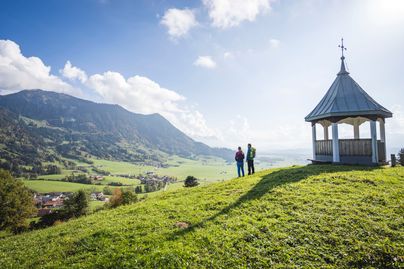 Zwei Wanderer stehen auf der Gebhardshöhe vor dem Pavillon und Blicken Richtung Grünten.
