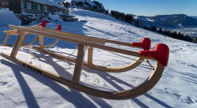 Zwei Schlitten liegen im Winter vor der Grüntenhütte in Rettenberg. Die Grüntenhütte liegt auf 1.477 Metern in traumhafter Lage unterhalb des Grüntengipfels. Von Kranzegg erreicht man die Einkehrhütte über einen gut ausgebauten Alpweg oder einen idyllischen Wald- und Wiesenweg