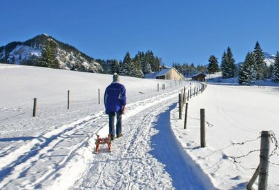Ein Mann ist mit seinem Rodel auf dem schneebedeckten Winterwanderweg unterwegs zum Sonthofener Hof.