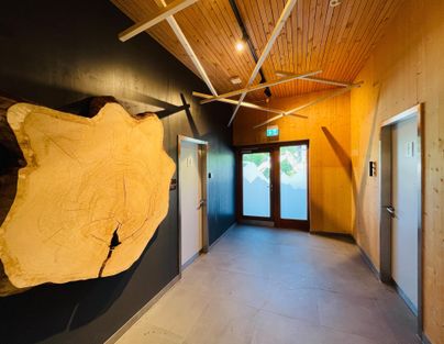 Ein heller Flur mit Holzverkleidung und modernen Elementen. An der Wand ist ein großes Holzstück zu sehen, und es gibt Türöffnungen zu den Seiten.