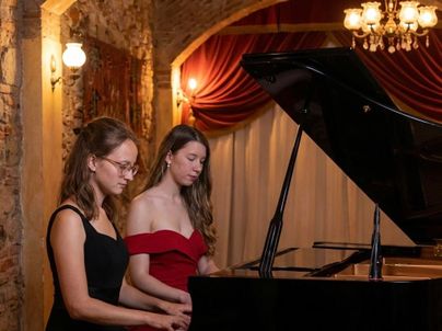 Zwei Frauen spielen gemeinsam am Klavier in einem elegant dekorierten Raum. Die Atmosphäre ist festlich und die Beleuchtung ist warm und einladend.