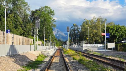 Ein Blick auf ein Bahngleis mit einem Bahnhof im Hintergrund. Die umliegenden Bäume und Berge schaffen eine malerische Atmosphäre.