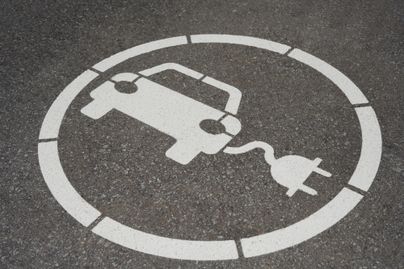 Ein Parkplatz für Elektroautos mit einem Symbol eines Autos und einem Stromstecker. Der Hintergrund ist asphaltiert.