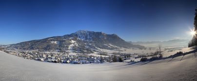 Winter Ortsansicht von der Gemeinde Rettenberg mit dem Grünten und den Allgäuer Hochalpen im Hintergrund.