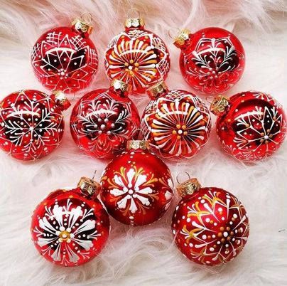 Eine Auswahl an roten Weihnachtsbaumkugeln mit verschiedenen kunstvollen Mustern in Schwarz und Weiß. Die Kugeln liegen auf einer weichen, hellen Unterlage.