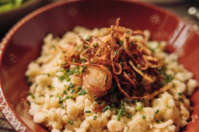 Ein köstlicher Teller mit Käsespätzle, garniert mit knusprigen Zwiebelringen und frischem Schnittlauch. Das Gericht ist in einer dekorativen Schüssel serviert.
