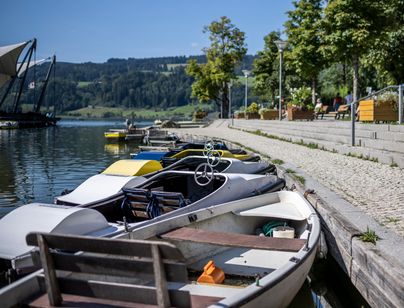Ein Papa läuft an einem schönen Sommertag mit dem Kinderwagen am Bootshafen des Großen Alpsees bei Immenstadt entlang.