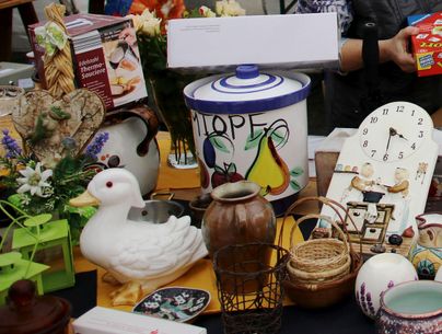 Ein attraktiver Marktstand mit verschiedenen Antiquitäten und Handwerksgegenständen. Zu sehen sind unter anderem eine bunte Kanne, Keramik und eine Uhr.