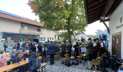 Eine musikalische Darbietung im Freien mit vielen Menschen, die sich versammelt haben. Die Band steht unter einem Baum und spielt in einer gemütlichen Atmosphäre.