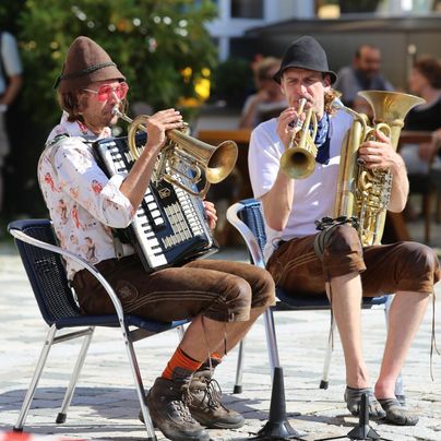 Zwei Musiker sitzen auf Stühlen und spielen eine fröhliche Melodie. Der Mann links spielt Akkordeon, während der Mann rechts eine Tuba spielt.