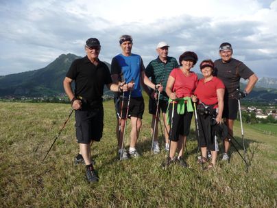 Eine Gruppe von sechs Menschen steht auf einer Wiese, umgeben von hügeliger Landschaft. Sie halten Wanderstöcke und lächeln kamerafreundlich.