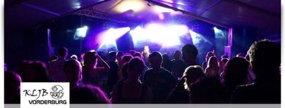 Eine lebhafte Veranstaltung mit vielen Menschen unter einem Zelt. Bunte Lichter erhellen die Atmosphäre und sorgen für eine festliche Stimmung.