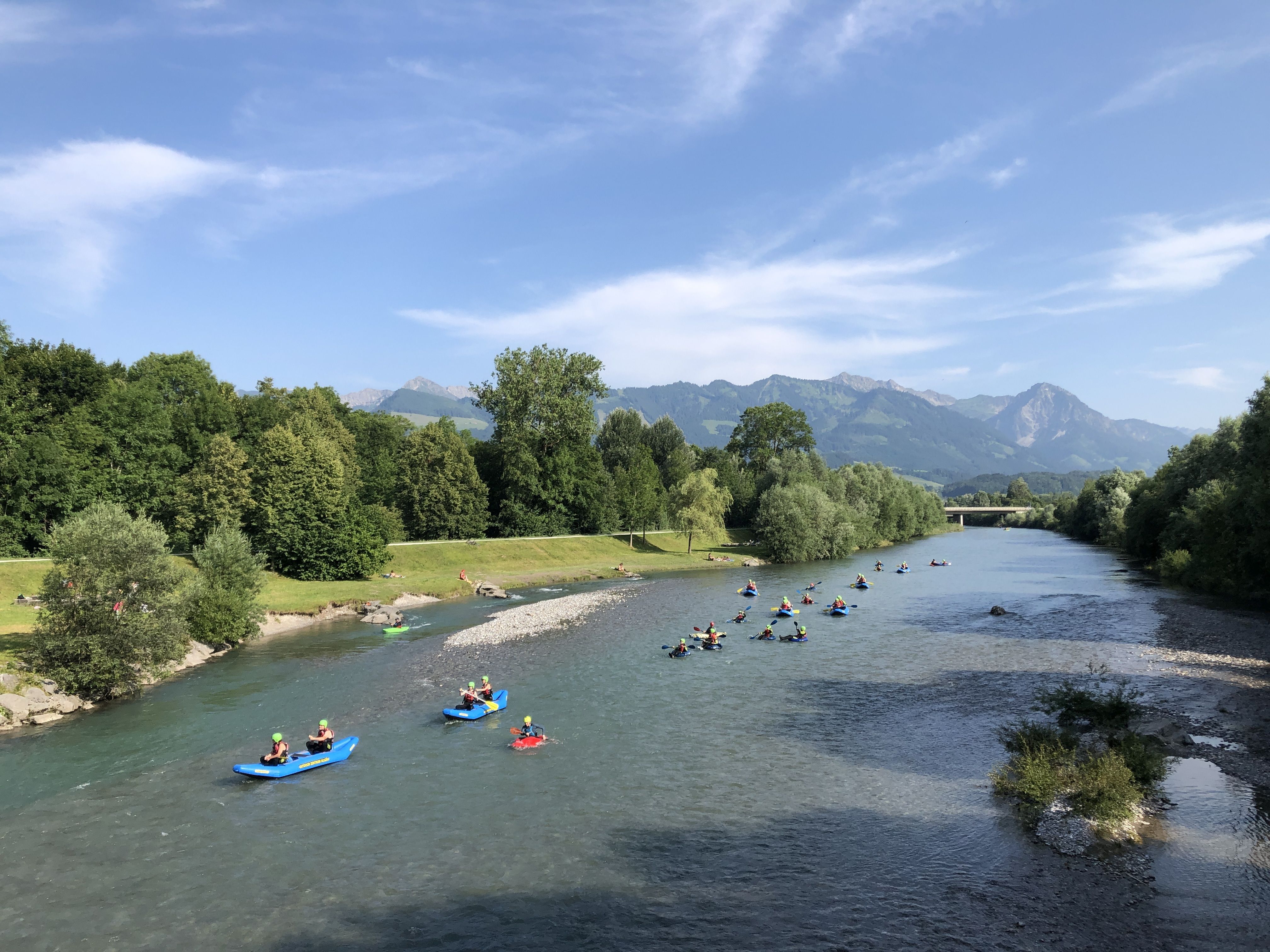 Eine Gruppe von Leuten fährt beim Rafting mit verschiedenen Booten die Iller entlang.