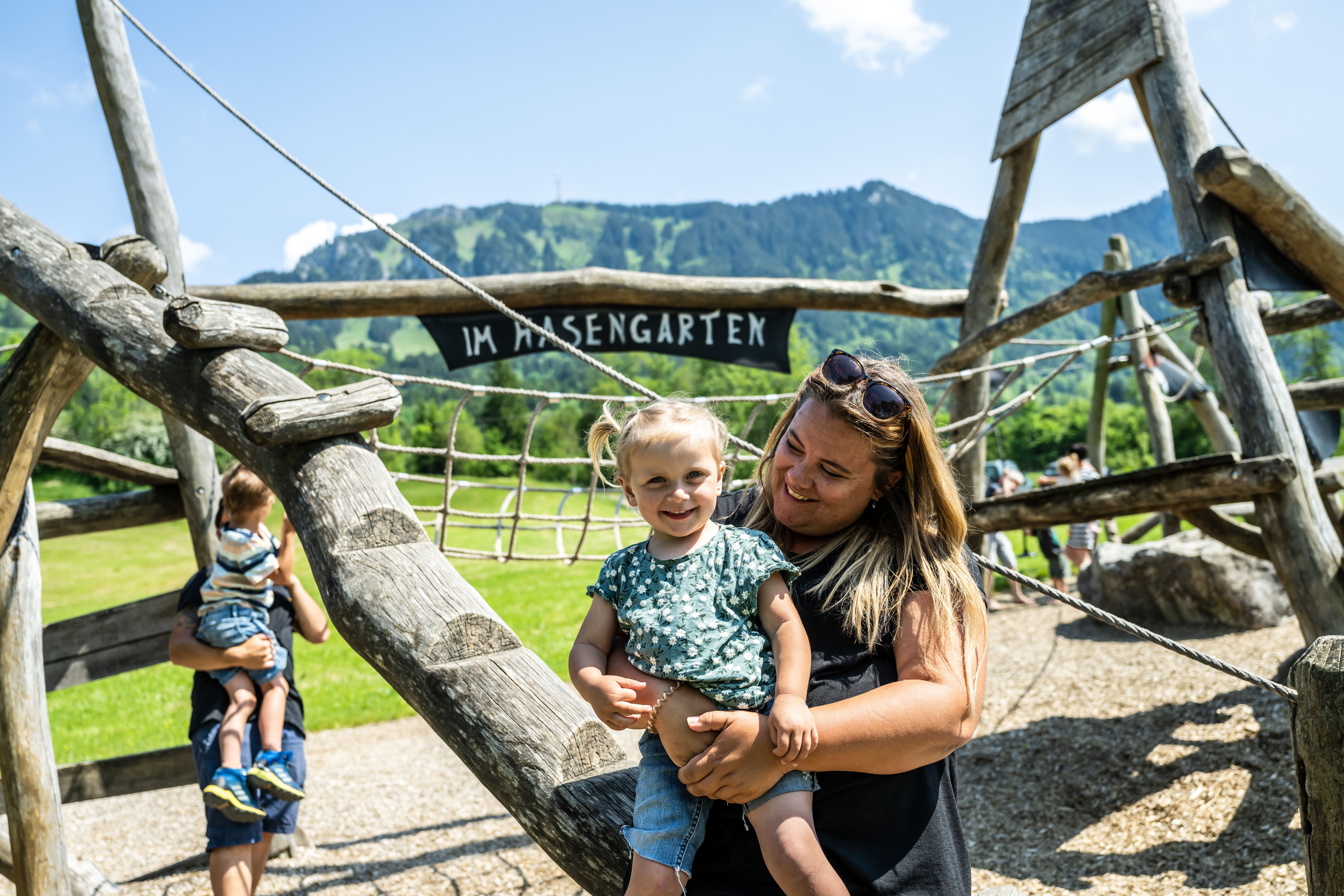 Ein Familie spielt auf dem Spielplatz Hasengarten in Rettenberg. Im Vordergrund sind Mutter und Tochter zu sehen, im Hintergrund beginnen Vater und Sohn auf einem Klettergerüst zu klettern.