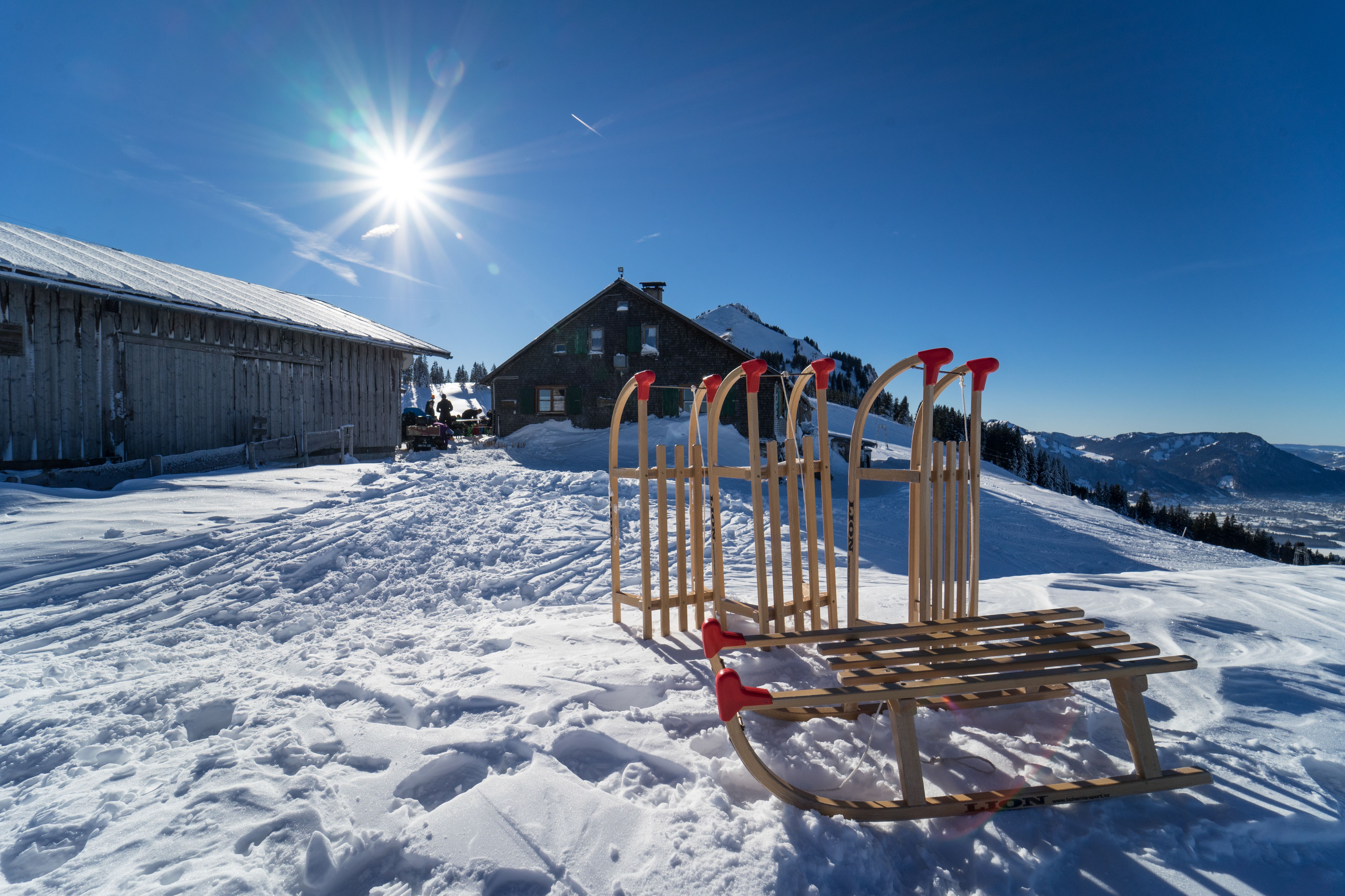 Vier Schlitten stehen bzw. liegen vor der Grüntenhütte im Winter. Auf traumhafter Lage liegt die Grüntenhütte auf 1.477 Metern unterhalb des Grüntengipfels. Von Kranzegg (Rettenberg) kann die Hütte gut über einen Alpweg oder idyllischen Wald- und Wiesenweg erreicht werden.