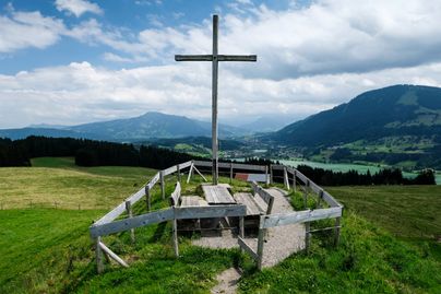 Auf dem Bild ist das Gipfelkreuz oberhalb der Siedelalpe mit Blick auf den Großen Alpsee zu sehen. Da es sich um ein leicht erreichbares Gipfelkreuz handelt, ist es ein beliebtes Ausflugs- und Fotoziel bei Gästen und Einheimischen.