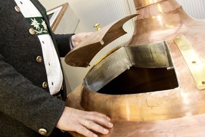Ein Braumeister öffnet den Deckel eines kupfernen Sudkessels. Der Kessel ist Teil eines traditionellen Brauprozesses.