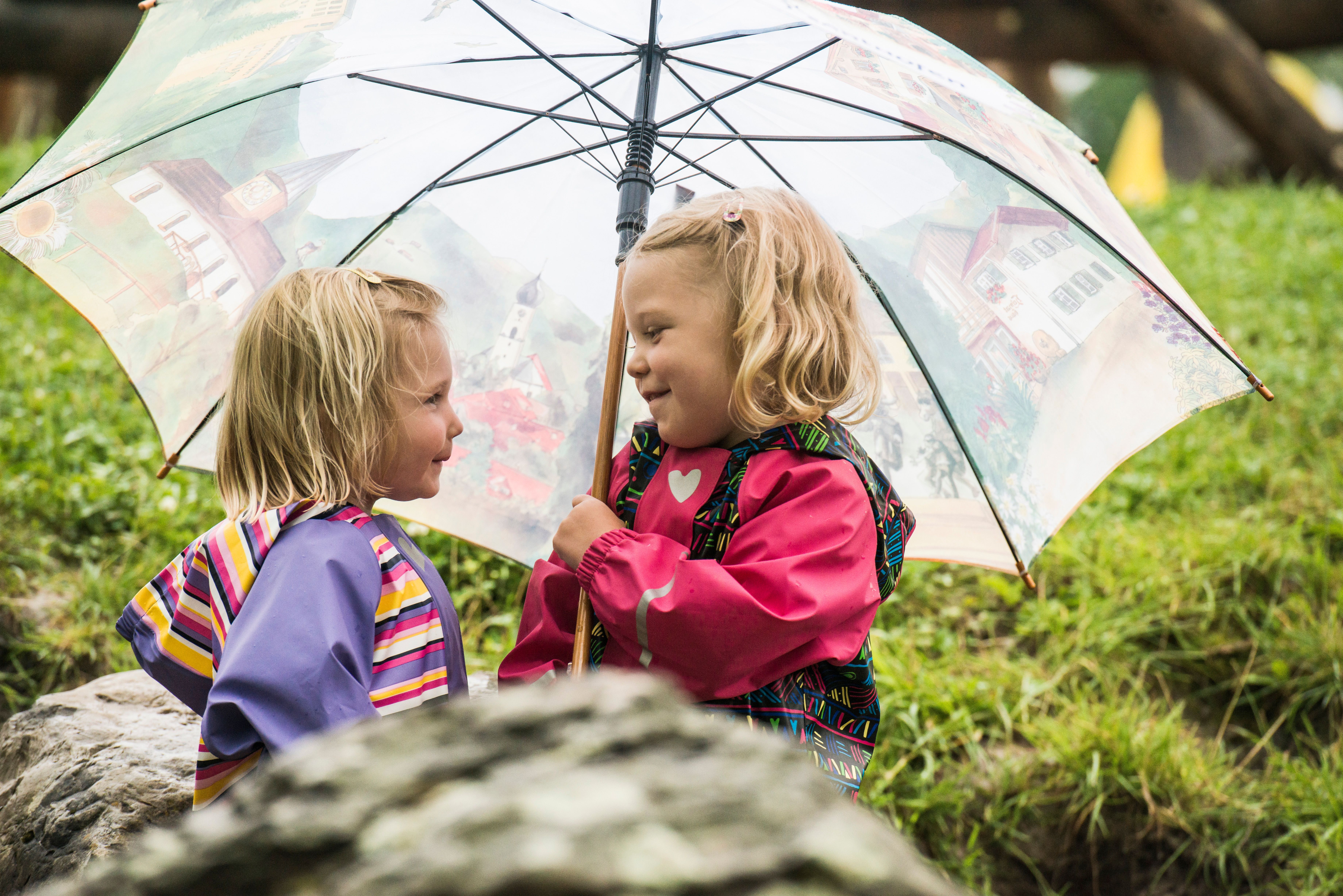 Zwei Mädchen spielen im Regen und stehen lachend unter einem Schirm.