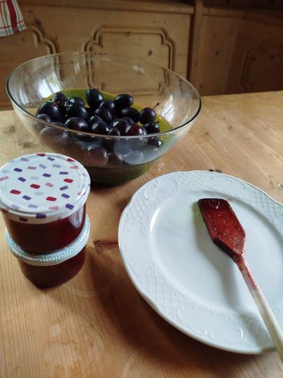 Ein Glas mit Trauben steht auf einem Tisch, daneben liegt ein Teller und ein Spatel mit Marmeladenresten. In der Nähe steht ein weiteres Glas mit roter Marmelade.